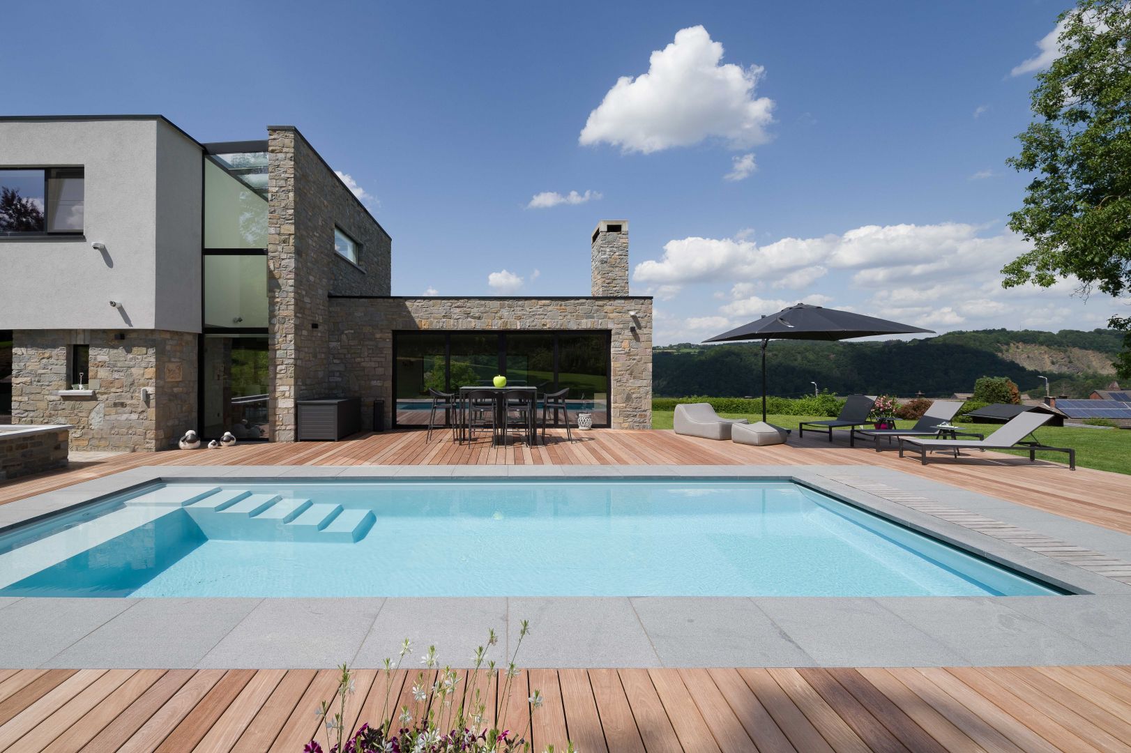 Full vinylester monoblok zwembad LPW La Plage 10 in Pearl Grey met houten terras en Covrex-afdekking bij een moderne natuurstenen villa.